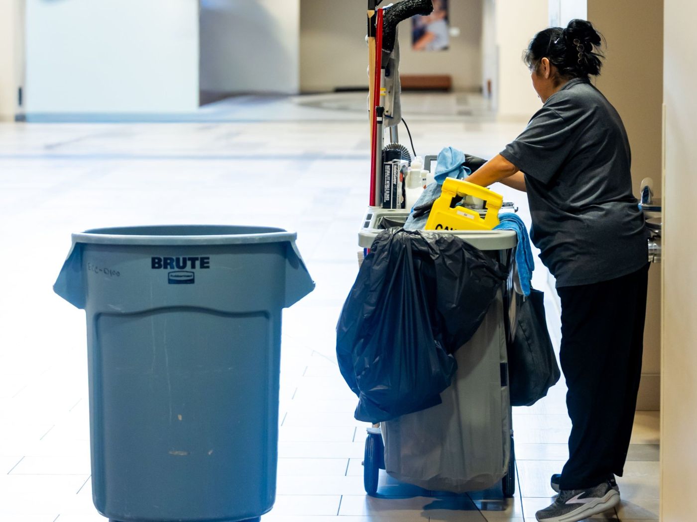 Cleaner restocking a janitorial cart in a corridor